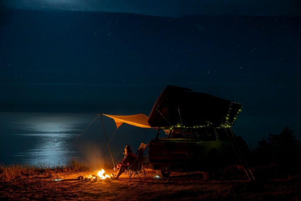 Camper sitting by campfire near lake at sunset enjoying peaceful camping moment