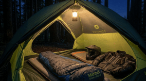 Marmot Crane Creek 2P tent pitched in a forest clearing next to an adventure motorcycle at sunrise.