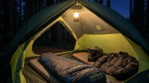Marmot Crane Creek 2P tent pitched in a forest clearing next to an adventure motorcycle at sunrise.