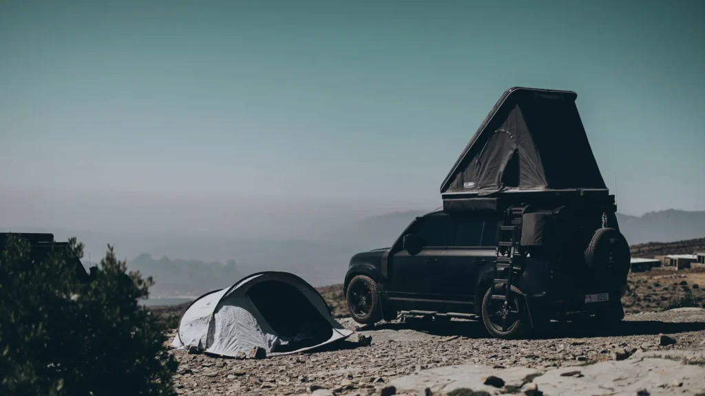 Can you tent camp in an RV site: The image shows a car with roof top tent on it, parked with another tent pitched on the ground in an RV site.