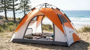 An orange Moon Lence pop up tent with all windows open for maximum ventilation at a beach campsite.