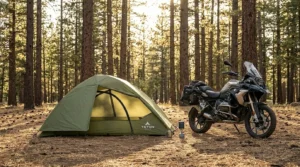 A TETON Sports Vista Quick Tent pitched in a forest clearing next to a motorcycle at sunset.
