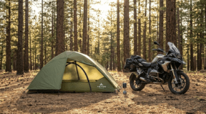 A TETON Sports Vista Quick Tent pitched in a forest clearing next to a motorcycle at sunset.