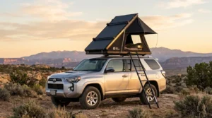 A black aluminum hard shell Arctwonder roof top tent set up on an SUV at sunset.