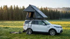 A side-opening hard shell Wildfinder rooftop tent set up on an SUV in a forest.